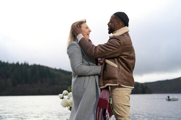 Smiling couple in warm clothing embracing by lake
