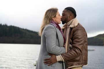 Obraz premium Happy couple in warm clothing kissing by river