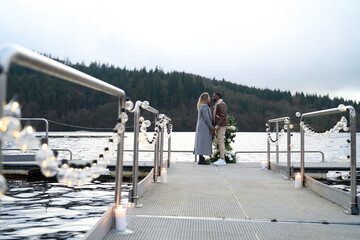 Happy couple in warm clothing standing face to face on decorated pier