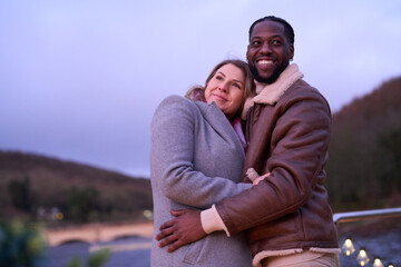 Obraz premium Smiling couple in warm clothing embracing by lake