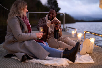 Smiling couple in warm clothing enjoying champagne on decorated pier