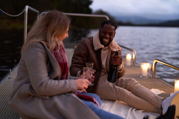 Smiling couple in warm clothing enjoying champagne on decorated pier