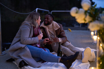 Smiling couple in warm clothing enjoying champagne on decorated pier