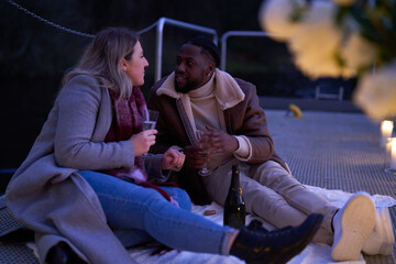 Smiling couple in warm clothing enjoying champagne on decorated pier