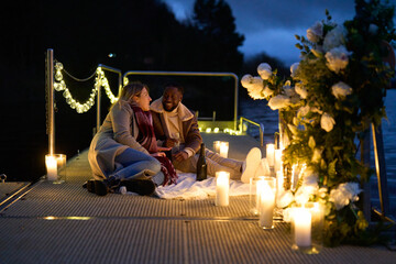 Smiling couple in warm clothing enjoying champagne on decorated pier at night