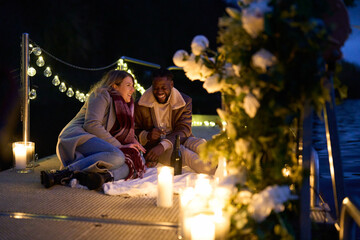 Smiling couple enjoying champagne on pier with candles and flowers at night