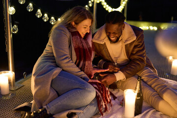 Smiling couple enjoying champagne on pier with candles at night
