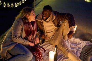 Smiling couple enjoying champagne on pier with candles at night