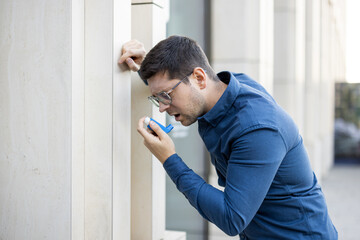 Plakat A man with an inhaler leans against a wall, looking concerned as he takes his medication. This could represent anxiety or breathing issues.