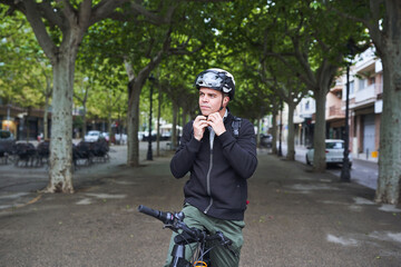 Man fastening helmet before riding electric bicycle in green urban area