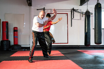 Instructor assisting man practicing kung fu in gym