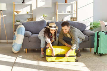 Couple enthusiastically packs their suitcase in preparation for their upcoming summer vacation. Man...