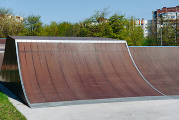 modern skate park, brown skateboard ramp outdoors in city park in summer for skateboarding, roller skating and bicycle riding, extreme sport