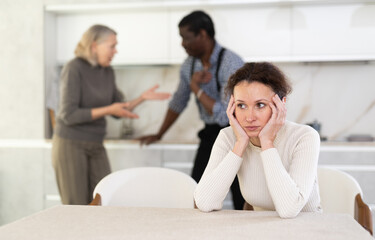 Upset woman tired of domestic quarrel. Husband and mother in law quarreling in the background