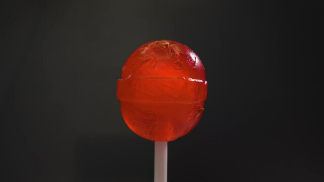 Red lollipop candy on a white plastic stick, on a black background. Sweet round candy spins on a turntable in motion
