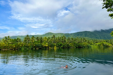 man swims in tropical river in wild jungle