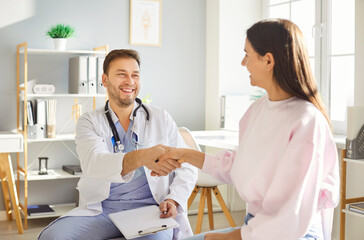 Obraz premium Smiling and positive male doctor or nurse shakes hands with a patient during a medical appointment in a hospital or clinic. Healthcare, care, and trust in professional consultation.