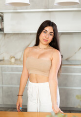 Young positive brunette woman posing in kitchen interior in apartment
