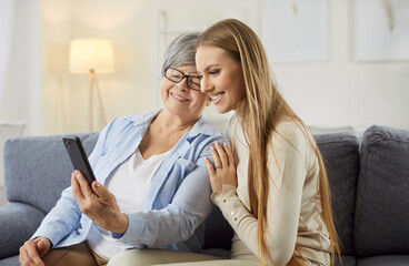 Female happy two generations of women family watching phone screen pictures online, mom or granny...