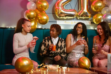 Fototapeta premium Group of female friends sitting with cocktails on sofa during birthday party