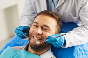 Close-up portrait of male patient sitting in modern dentistry clinic during medical check up in medical center. Dentist examining young man teeth with dental tools. Dental health care.