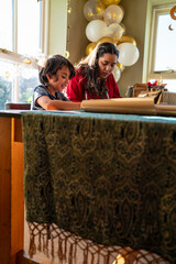 Young woman with little sister wrapping gifts for Eid Celebration