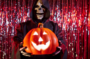 Close-up of grim reaper holding pumpkin during halloween party, featuring skeleton and terrible...