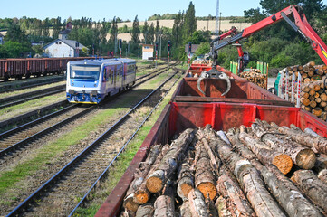 Heavy machinery loads logs onto train cars at a railway yard, depicting the industrial process and logistical complexities involved in transporting raw materials