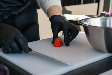 chef cutting fresh red ripe strawberries with a knife on a white cutting board