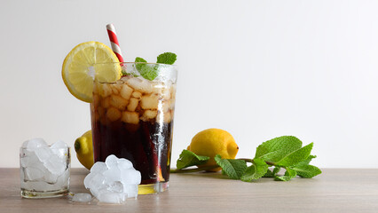 Refreshing cola drink with mint and lemon on wooden table