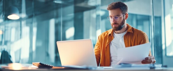 The focused man working on a laptop in a modern office environment.