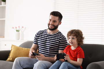 Happy father and his son playing with game controllers together on sofa at home