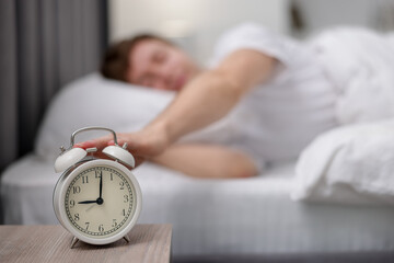 Man turning off alarm clock in bed indoors, selective focus