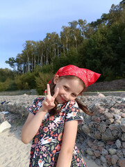 Russia, Kaliningrad, cute little girl standing and posing on the Baltic sea shore, she wearing dress with flowers and red handkerchief - bandana on the head