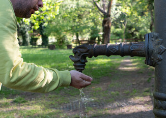Fototapeta premium Man Drinking from Elegant Vintage Street Fountain in Park