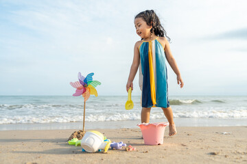 Cheerful adorable little girl having fun outdoor and playing with sand with beach kid toys on the...