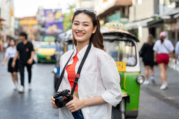 Young Asian woman traveling backpacker in Khaosan Road outdoor market in Bangkok Thailand. Happy female tourist walking in the downtown street traditional market