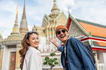 Young Asian couple man and woman traveling backpacker walking in temple at Bangkok Thailand. Happy couple tourist walking in the downtown street. Holiday vacation time tourist