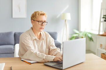 Thoughtful focused senior mature businesswoman working at laptop in office, busy using online app,...