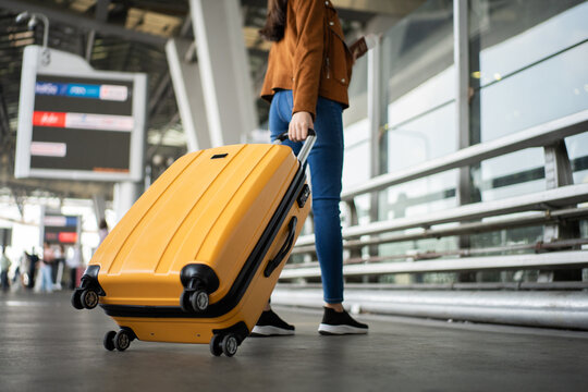 Close up of unrecognized woman tourist walking with her luggage through international airport terminal during holiday trip, female tourist rolling suitcase alone.