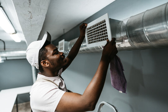 Maintenance worker adjusts air vent in modern basement room during the afternoon