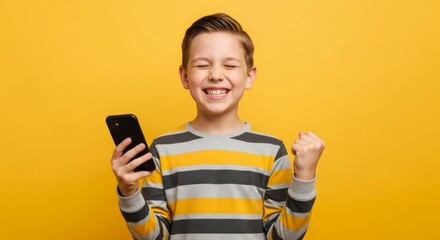 Excited boy holding smartphone celebrating success on yellow background happy child phone