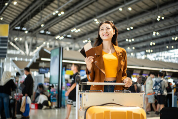 Fototapeta premium happy young asian woman traveler holding boarding pass ticket, passport and smartphone at the airport terminal with her luggage and smiling at camera, cheerful tourist female having holiday trip.
