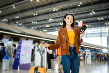 happy young asian woman traveler holding boarding pass ticket, passport and smartphone at the airport terminal with her luggage and smiling at camera, cheerful tourist female having holiday trip.