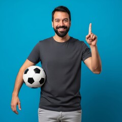 Fototapeta premium Man holding soccer ball pointing up football player with beard and gray shirt sport