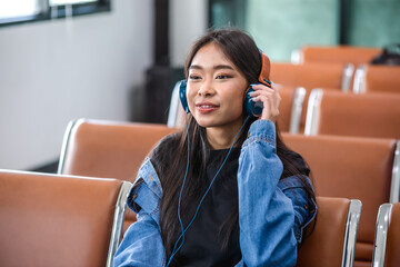 Young Asian traveler woman listening music from headphones waiting in airport
