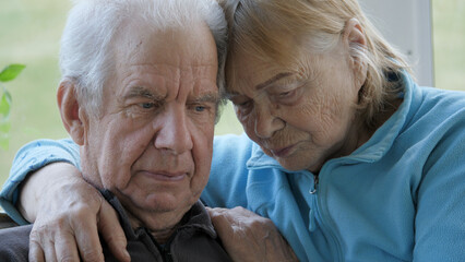 Elder old couple together hugging and with sad look silently looking down in nursing home. Lonely people without care and attention at home. Support and helping hand. Face with wrinkles and gray hair