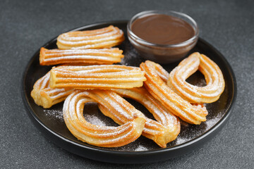 Traditional spanish dessert churros, fried dough pastry dusted with powdered sugar and chocolate sause on black background. Street food, sweet snack, homemade dessert.