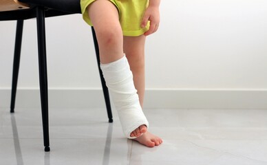 Child standing near the chair with a leg in a cast, showing signs of recovery after an injury.