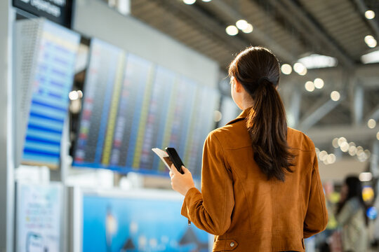 Portrait of confident young businesswoman smiling at camera ready traveling business trip with holding passport with ticket boarding pass and smartphone at the international airport terminal.